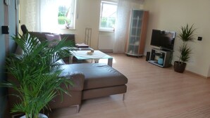 A living room with a sofa, coffee table, TV, and potted plants. - Spacious vacation apartment for families, fitters, cyclists, Legoland (Günzburg)