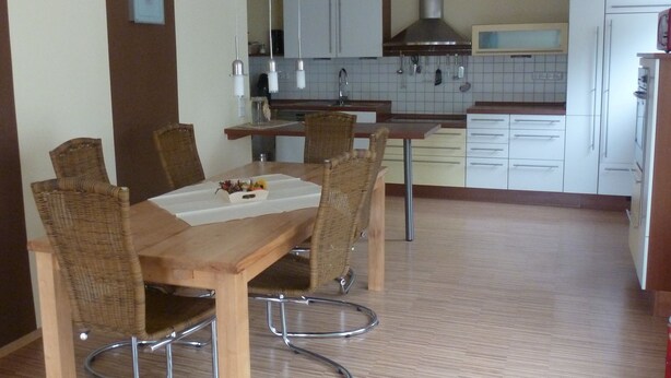 A modern kitchen with white cabinets, a stainless steel range hood, and a dining area with a wooden table and wicker chairs. - Spacious vacation apartment for families, fitters, cyclists, Legoland (Günzburg)