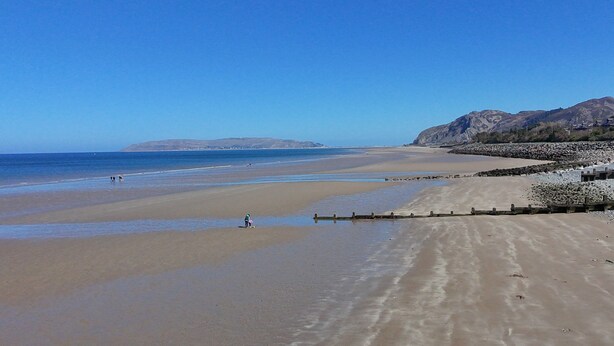 A wide sandy beach with a rocky shoreline and mountains in the background.