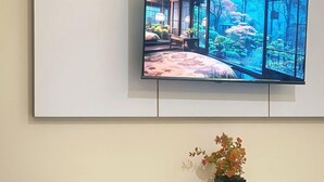 Una habitación moderna con una televisión de pantalla plana en la pared, un escritorio blanco y una pequeña planta en maceta.
