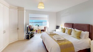 A hotel room with a large bed, a TV, a desk, and a window with a view of the sea. - Waters Edge - Three Bedroom Cottage, Sleeps 6 (Deganwy)