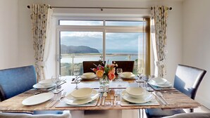 A dining table set for two with a view of the sea and mountains through the window. - Waters Edge - Three Bedroom Cottage, Sleeps 6 (Deganwy)