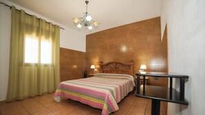 Une chambre à coucher avec un lit, deux tables de chevet avec des lampes, une tête de lit en bois, un lustre et une fenêtre avec des rideaux.