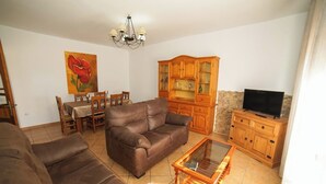 Un salon avec un canapé en cuir marron, une table basse en verre, des meubles en bois, une table à manger avec des chaises et un tableau accroché au mur.