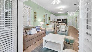 A living room with a sofa, ottoman, and coffee table, a kitchen with appliances, and a dining area with chairs. - New Listing! 30A Condo Close to Beach, Shopping and Dining! (Santa Rosa Beach)