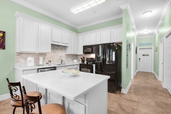 A kitchen with white cabinets, a central island, a refrigerator, and a microwave. - New Listing! 30A Condo Close to Beach, Shopping and Dining! (Santa Rosa Beach)