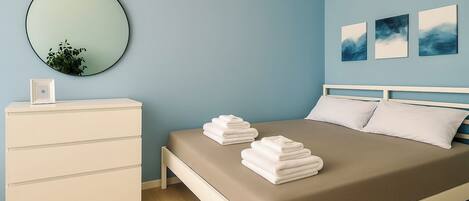 Une chambre à coucher avec un lit, une commode, un miroir et des œuvres d’art accrochées au mur.
