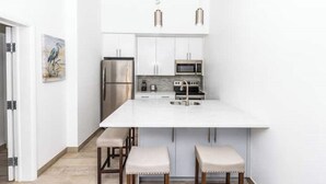 A modern kitchen with white cabinets, stainless steel appliances, and pendant lighting. - Buttonwood Lodge Unit #3 (Kew Town Settlement)
