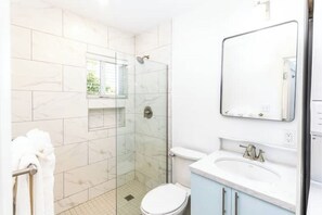 A bathroom with a glass shower enclosure, a toilet, and a sink with a mirror above it.