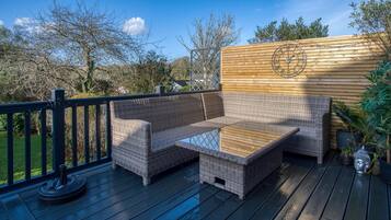 Relax on the deck with a wicker sofa and small table, surrounded by lush greenery.