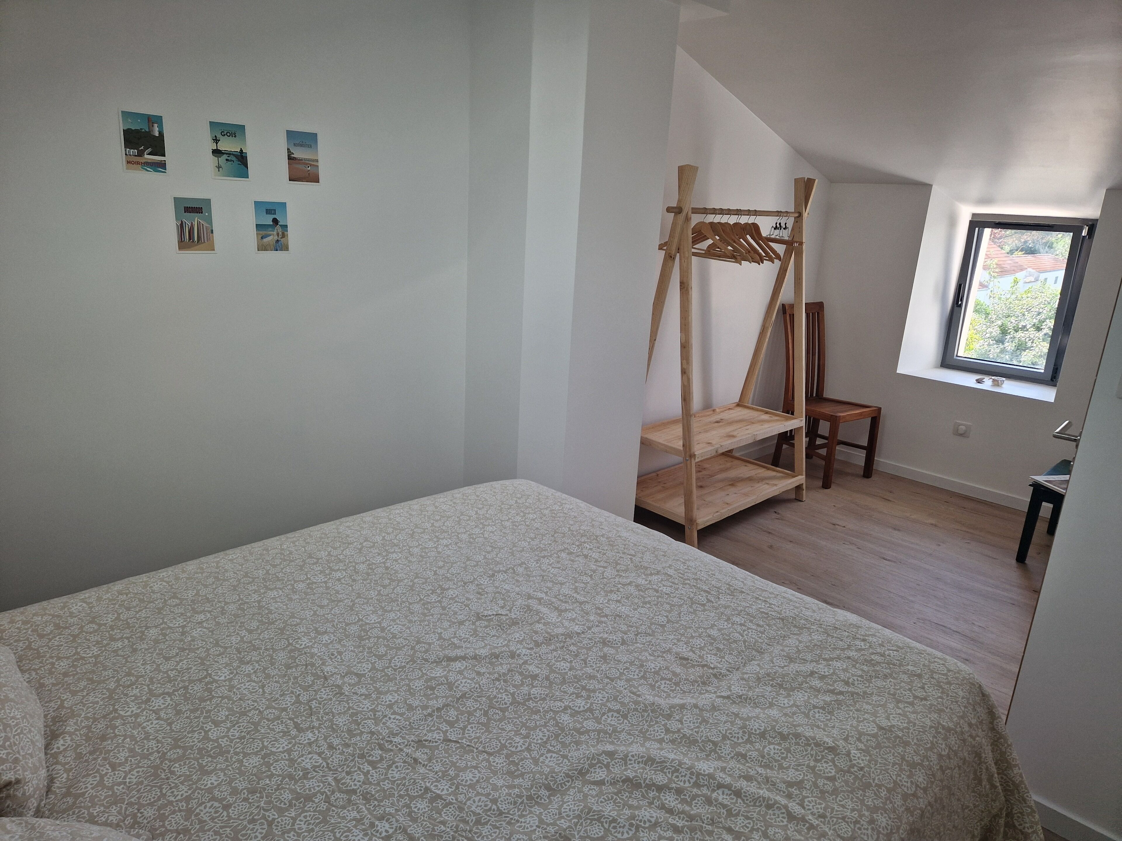 A bedroom with a bed, a wooden shelf unit, a chair, and a window.