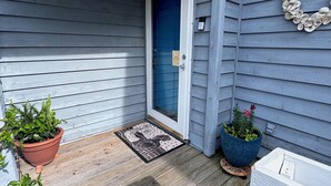 A wooden deck with a blue door, potted plants, and a white bench.