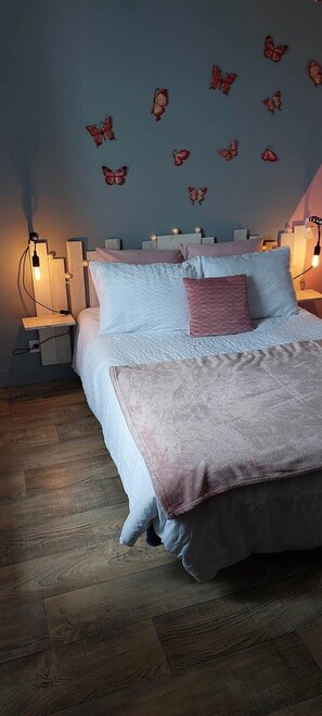 A bedroom with a bed, two bedside tables, a wall-mounted lamp, and butterfly wall decals.