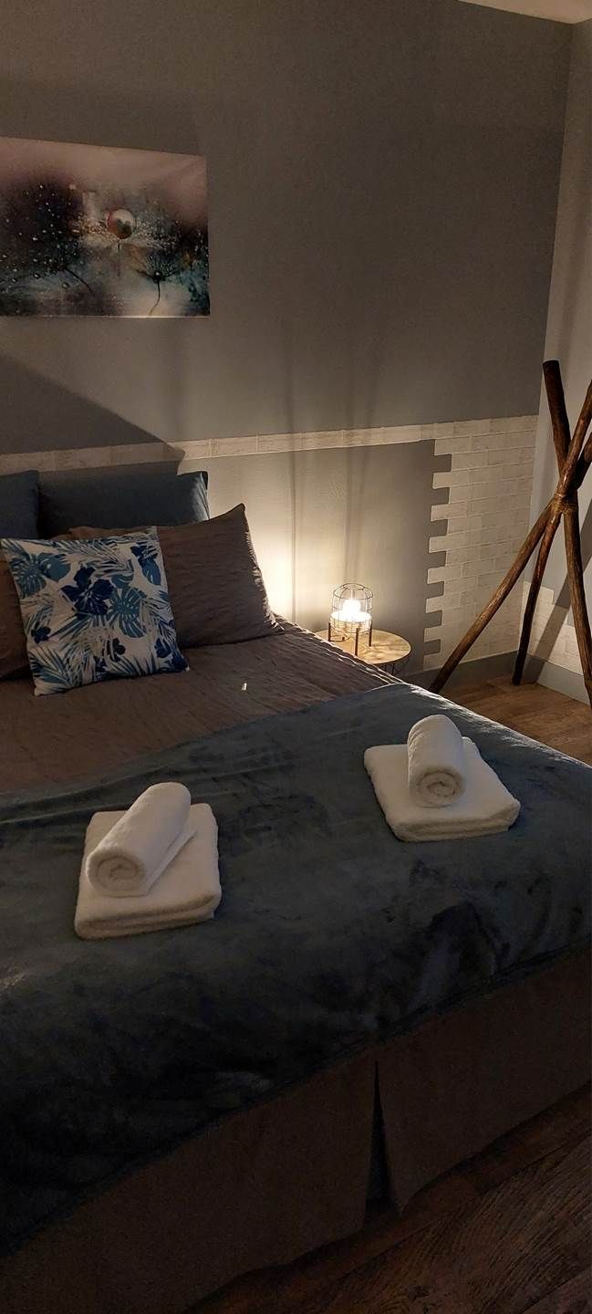 Une chambre à coucher avec un lit, des oreillers, une table de chevet avec une lampe et un tableau accroché au mur.