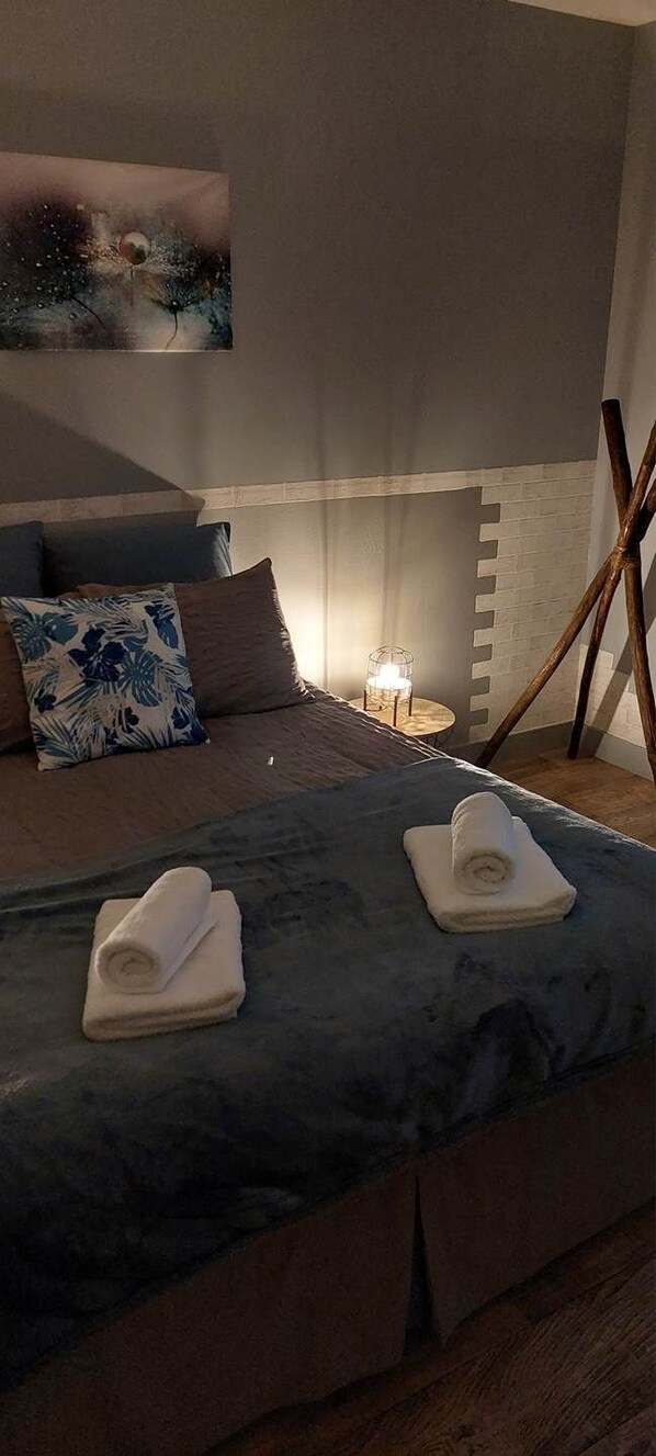 A bedroom with a bed, pillows, a bedside table with a lamp, and a painting on the wall.