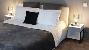 A neatly made bed with a dark headboard, white pillows, and a black accent pillow. There are two bedside tables with lamps, and the room has a wooden floor. - Country cottage, Verette cottage (Écueillé)