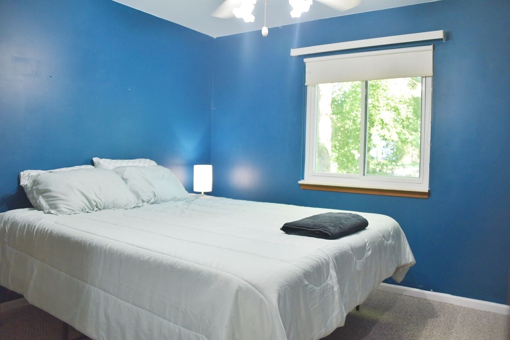 A bedroom with a bed, white bedding, a window with blinds, and a ceiling light.