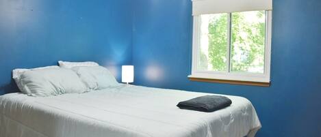 A bedroom with a bed, white bedding, a window with blinds, and a ceiling light.