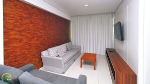 Una sala de estar moderna con un sofá gris, una mesa de centro de madera y un televisor de pantalla plana montado en la pared.