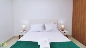 Habitación de hotel ordenada con una cama grande, dos mesitas de noche con lámparas, un armario de madera y una toalla verde sobre la cama.