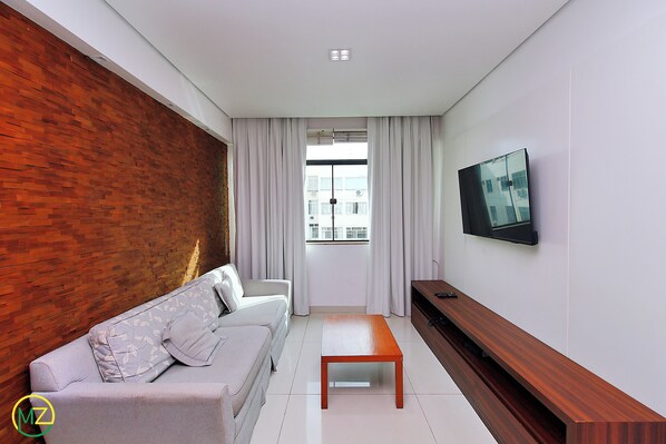 A modern living room with a sofa, a coffee table, a TV mounted on the wall, and a window with curtains. - RAUL POMPEIA III (Rio de Janeiro)