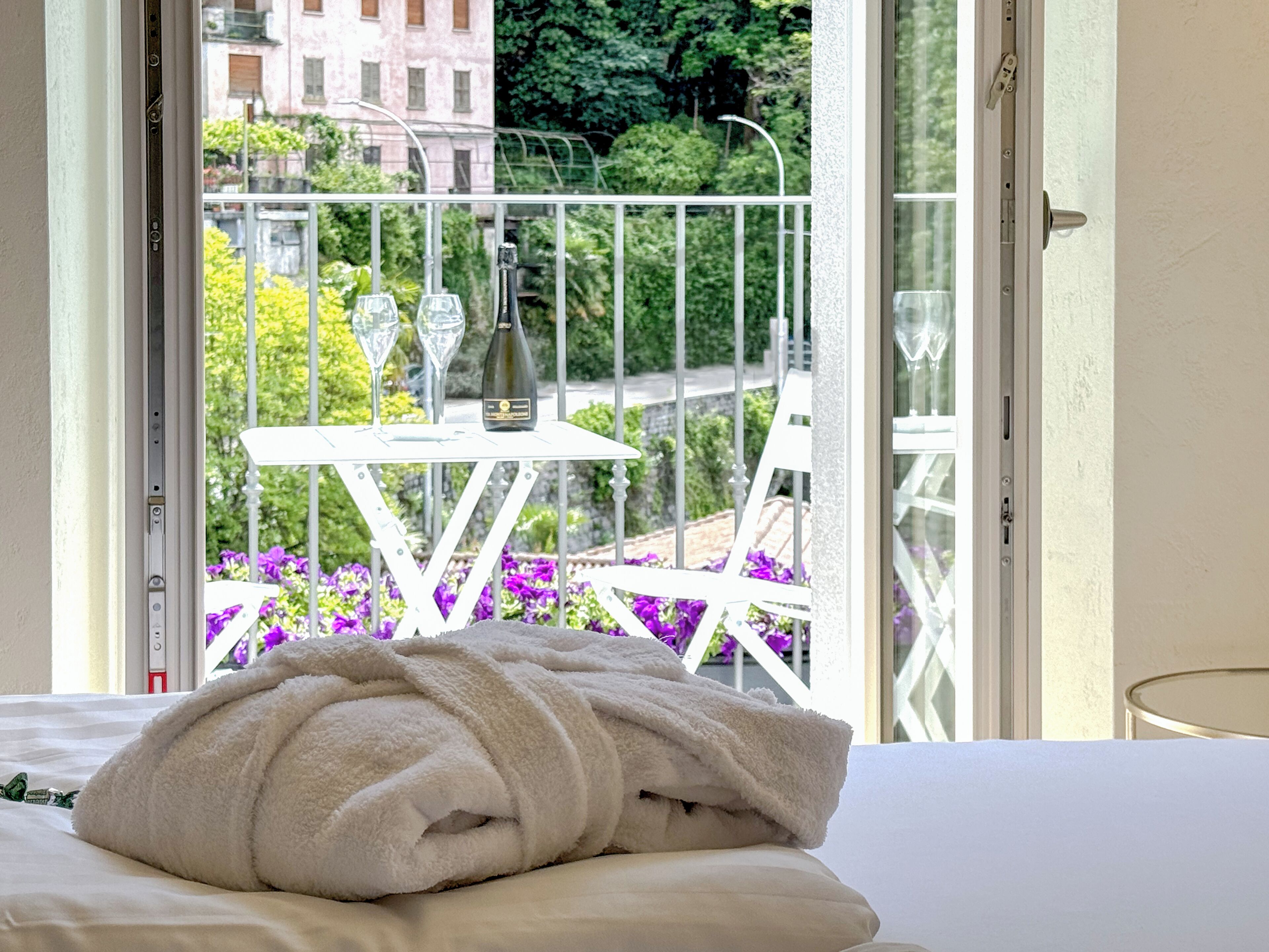 Een hotelkamer met een bed, een witte handdoek en een balkon met een tafel en stoelen.