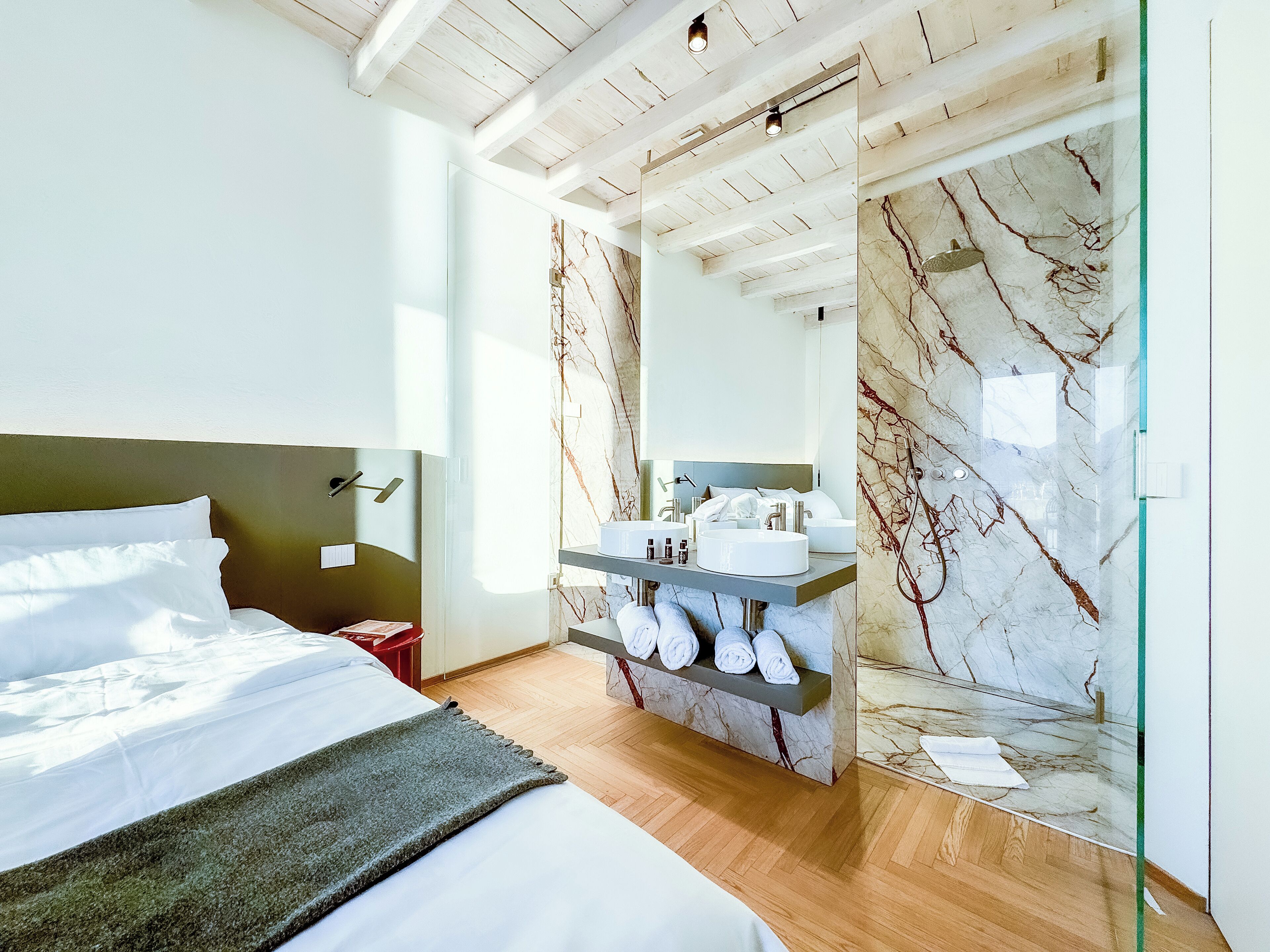A modern bedroom with a bed, a vanity with a marble backsplash, and a large mirror.