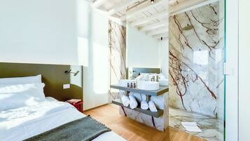 A modern bedroom with a bed, a vanity with a marble backsplash, and a large mirror.
