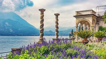 Vista de un lago con columnas de piedra, un pabellón y flores moradas.