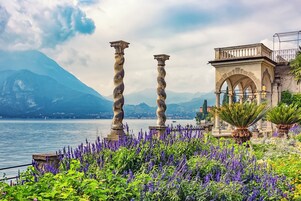Vista de un lago con columnas de piedra, un pabellón y flores moradas.