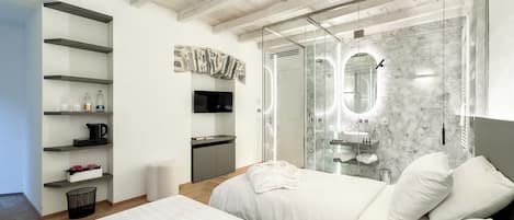 Un dormitorio moderno con una cama grande, un vestidor, un baño con ducha de vidrio y un televisor montado.