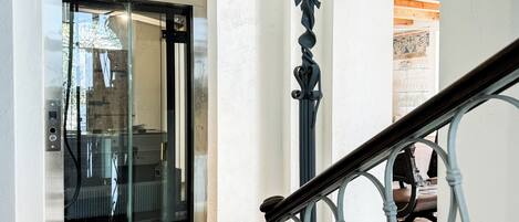 Una escalera con barandilla de metal y una puerta de cristal que da a una habitación con radiador y una alfombra estampada.
