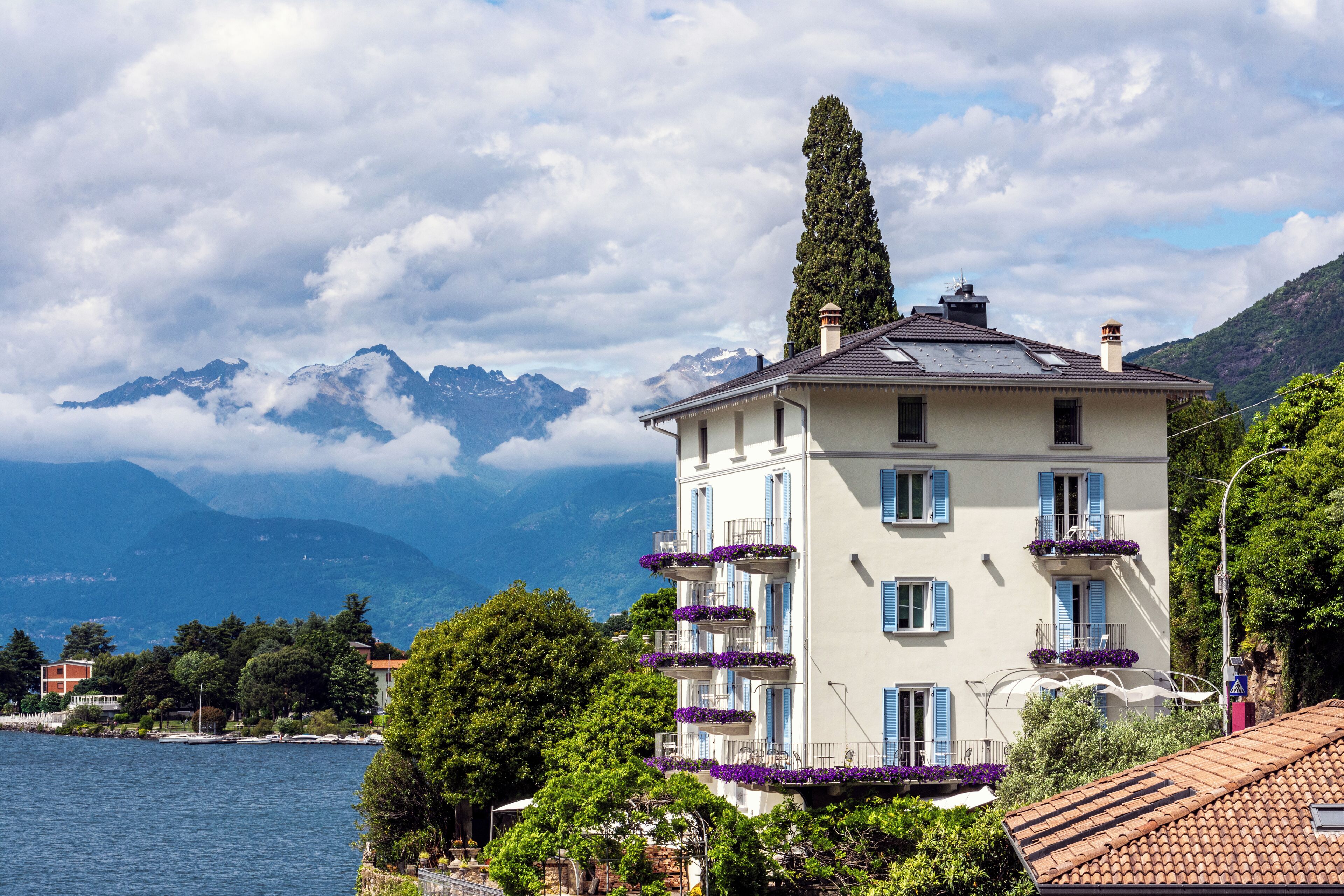 A multi-story building with balconies, located near a body of water with mountains in the background.