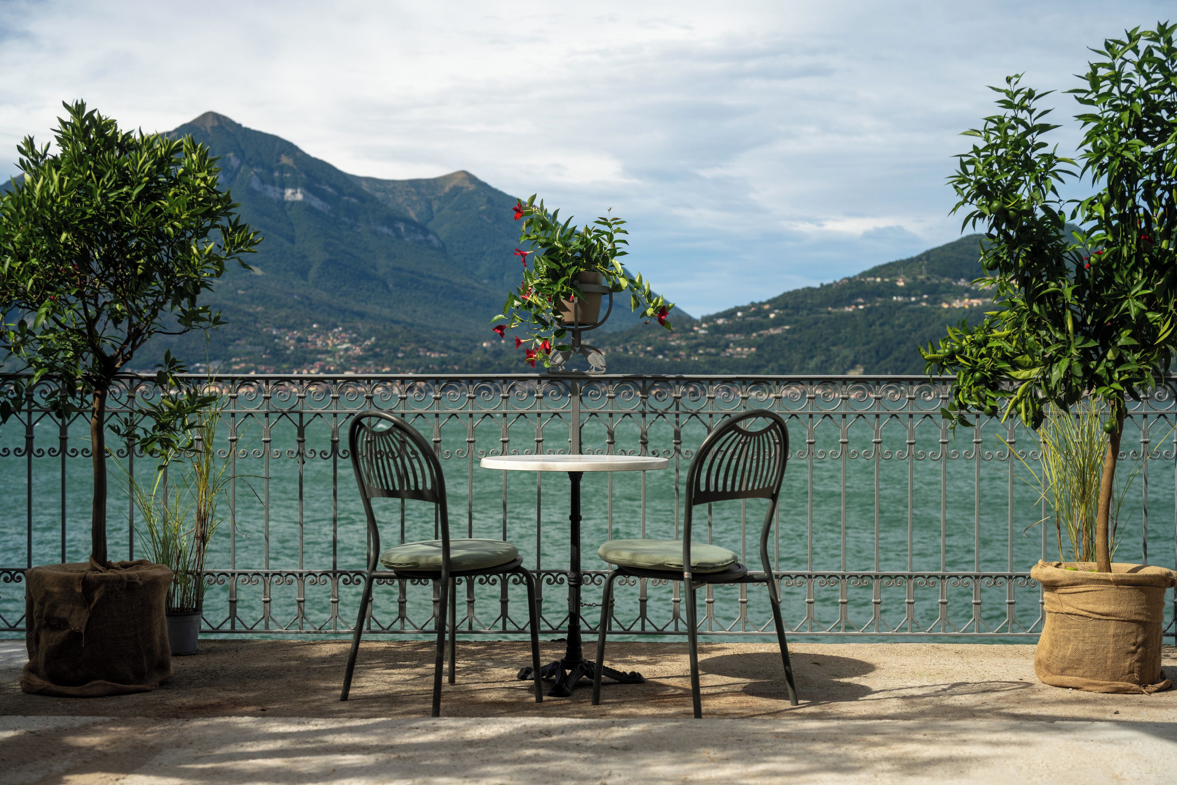 A terrace with two chairs and a table, a potted plant, and a view of a mountain and water.