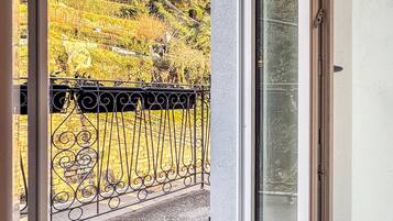 Un balcon doté d’une rambarde en métal, d’une porte vitrée et offrant une vue sur un paysage vallonné, avec des arbres et un bâtiment.