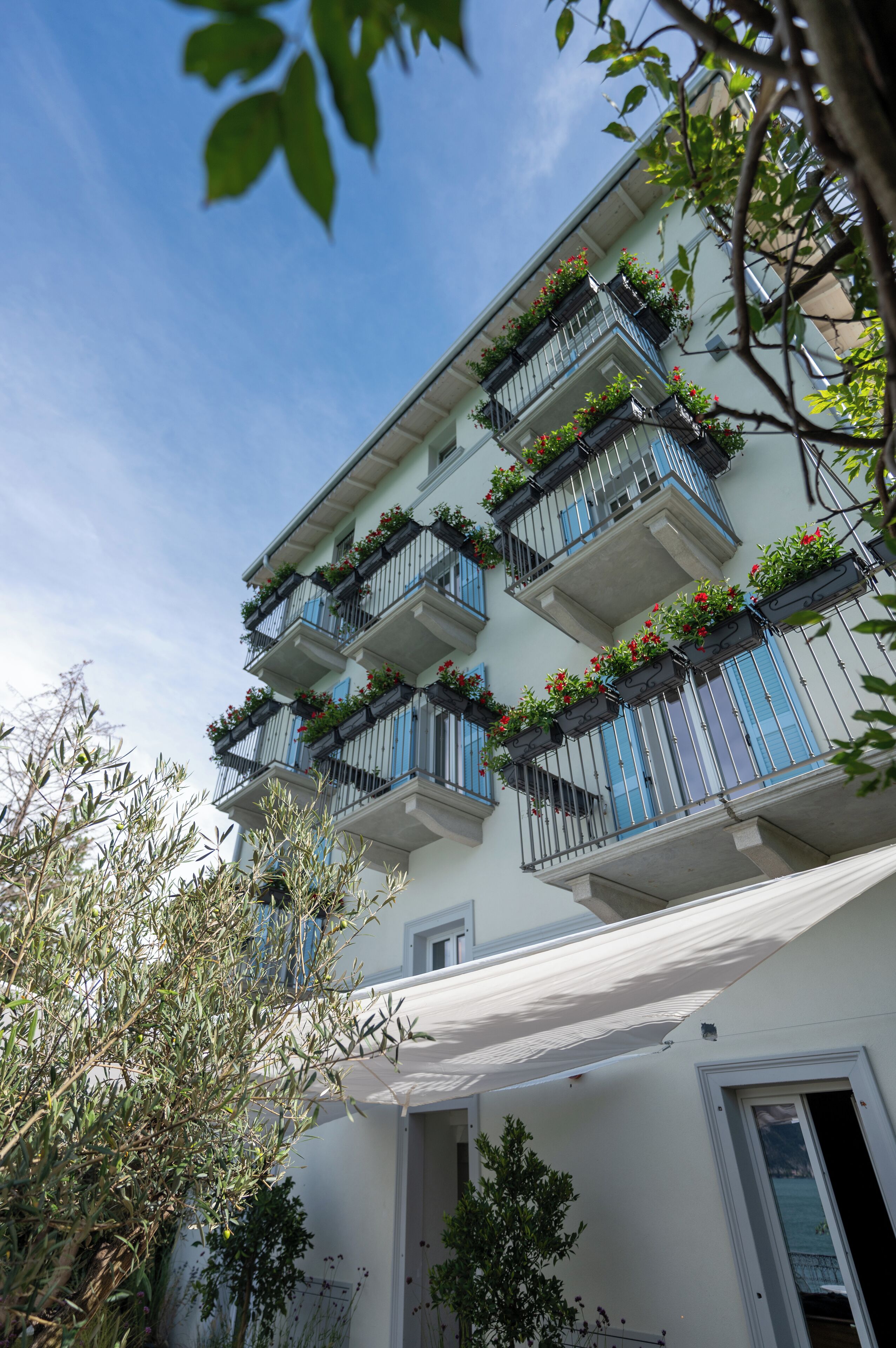 A multi-story building with balconies adorned with red flowers, a white facade, and a clear blue sky.