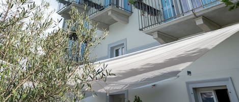 A multi-story building with balconies adorned with red flowers, a white facade, and a clear blue sky.