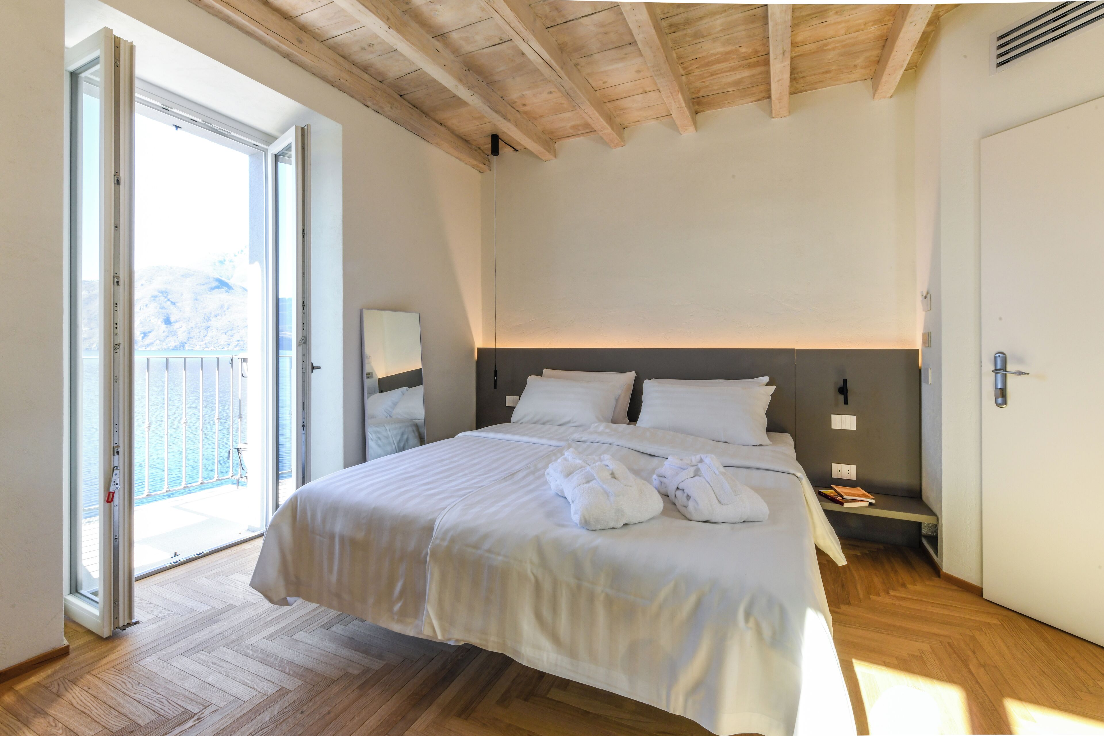 A bedroom with a large bed, a nightstand, a bedside table, a window with a view, and a wooden ceiling.