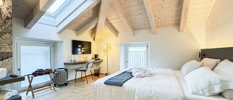 A bedroom with a large bed, a desk, and a chair, a skylight, and a stone wall.