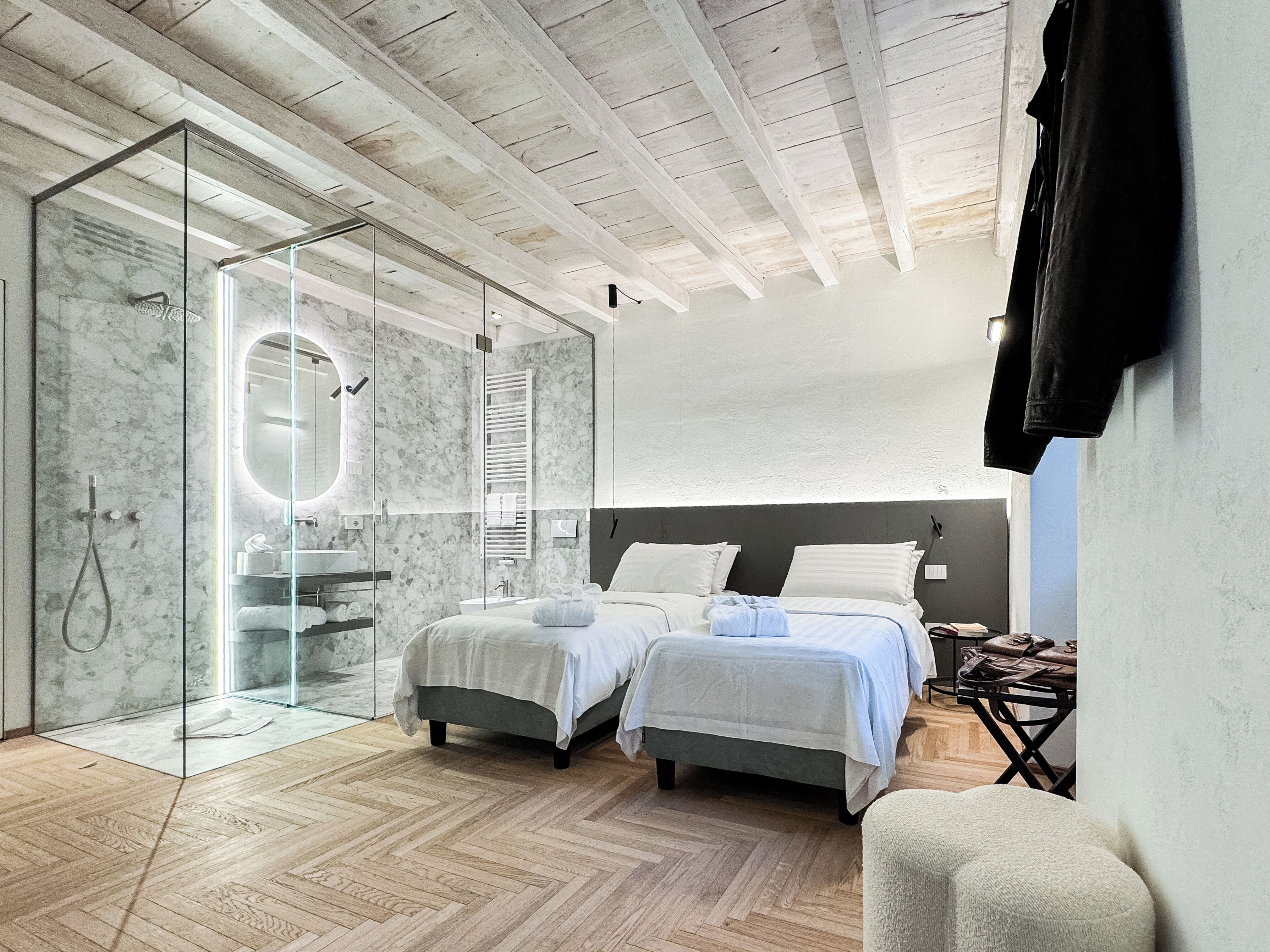 Une chambre moderne avec deux lits, un dressing et une douche en verre.