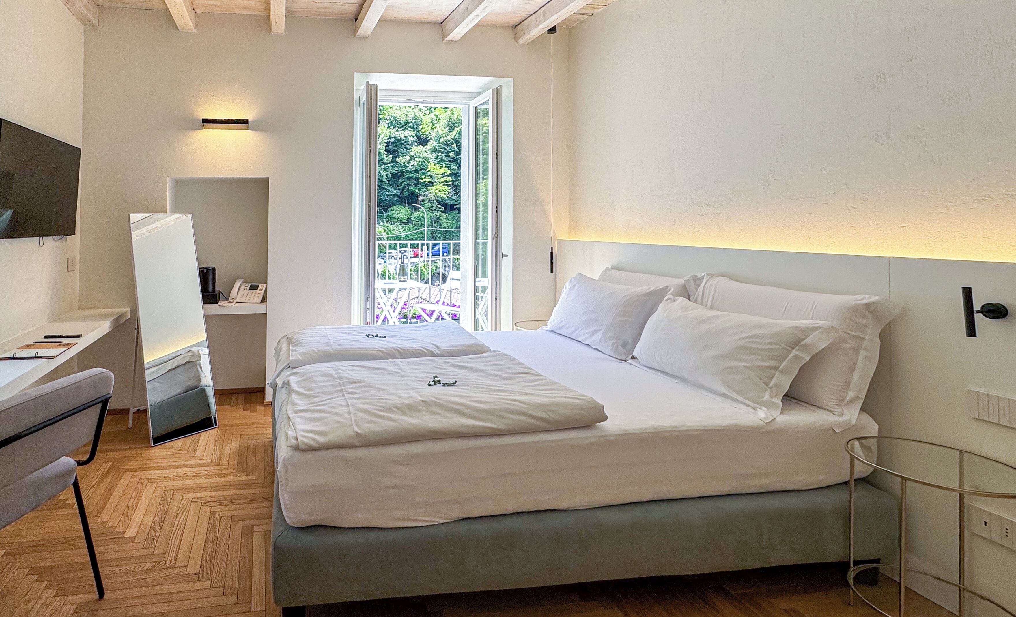 Un dormitorio con cama, escritorio, silla, teléfono y puerta que da a un balcón.