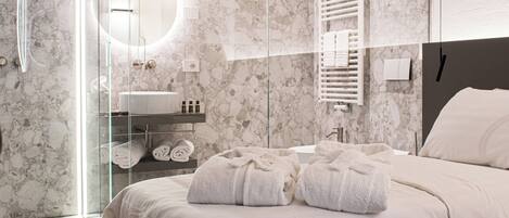 A modern bathroom with a glass shower enclosure, a marble wall, a sink, and a bed with towels.