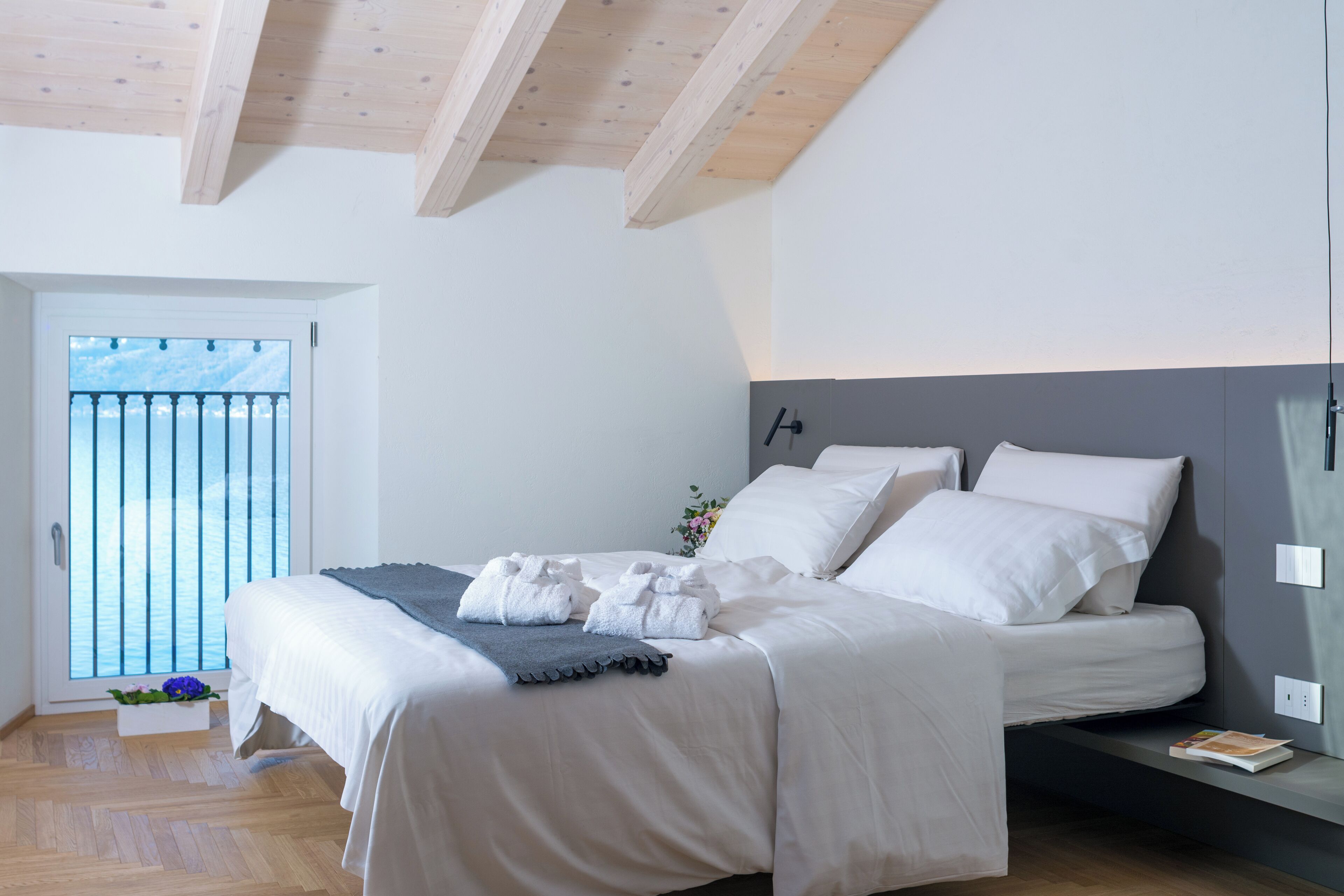 A bedroom with a bed, a bedside table, a window with a view, and a wooden ceiling.