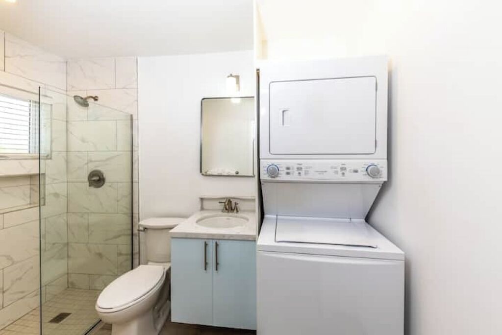 Un baño pequeño con ducha envuelta en vidrio, inodoro, lavamanos y lavadora y secadora integradas.