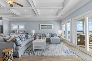 Un salon spacieux doté d’une grande fenêtre, d’un ventilateur de plafond et offrant une vue sur la plage.