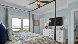 Een slaapkamer met een groot bed, een plafondventilator, een dressoir, een televisie en uitzicht op de oceaan.