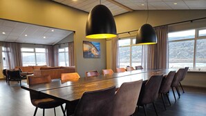 A conference room with a long table, chairs, and a sofa. There are large windows with curtains and a painting on the wall. - Long Valley Lodge  (Blönduós)