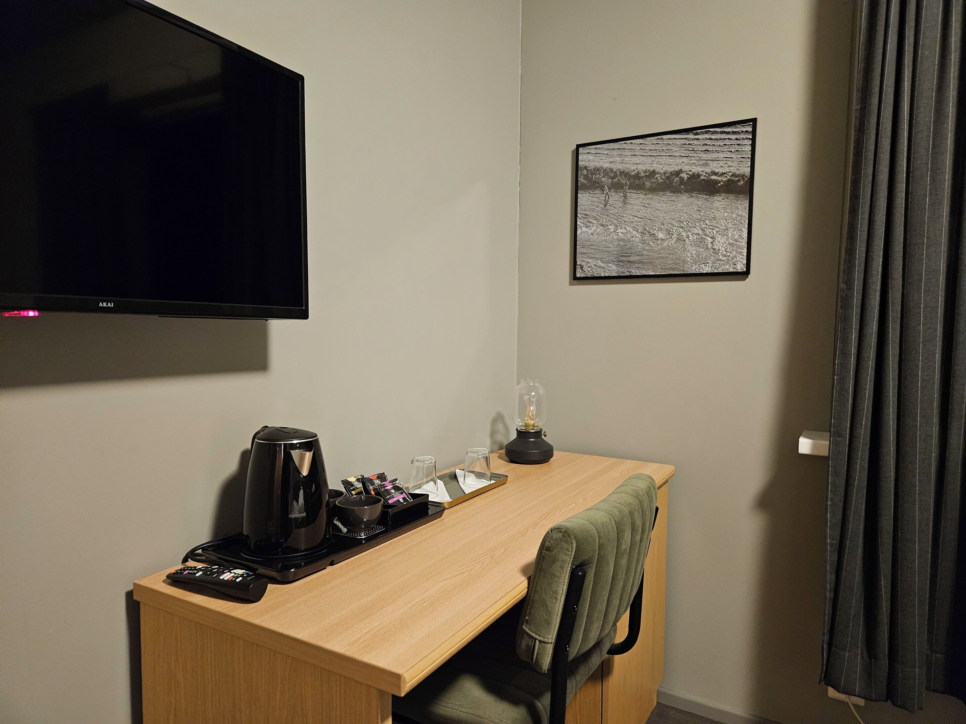 A hotel room with a wooden desk, a flat-screen TV, a coffee maker, a lamp, and a framed picture on the wall.
