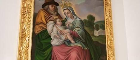 A framed painting of a religious scene with a halo, a child, and a woman in a green robe, mounted on a white wall.