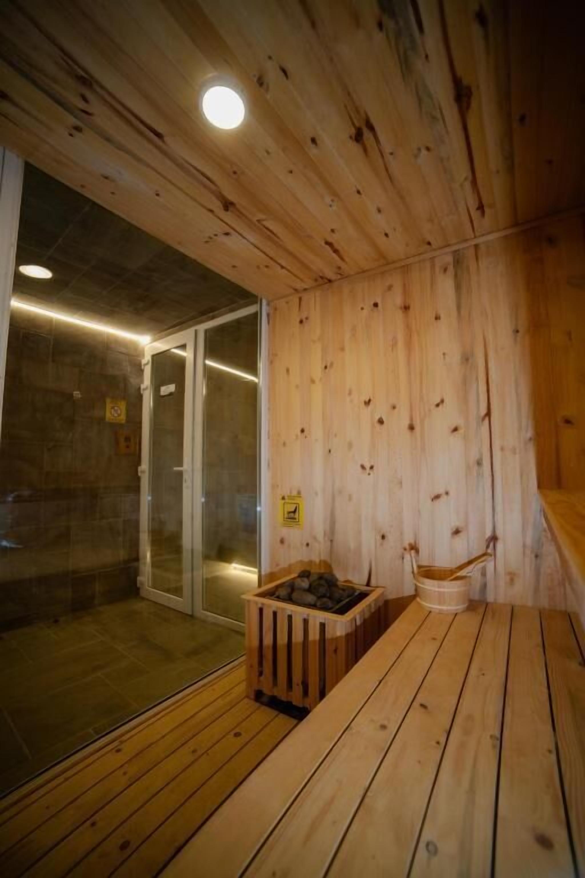 A wooden sauna room with a glass door, a wooden bench, and a stone basin.